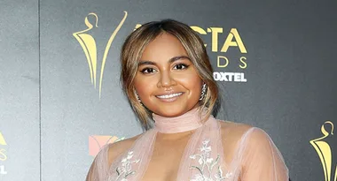 AICTAs red carpet event attendee in a sheer outfit smiles against a logo backdrop.