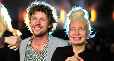 Two people standing close together, one smiling and the other appearing emotional with tears in their eyes.