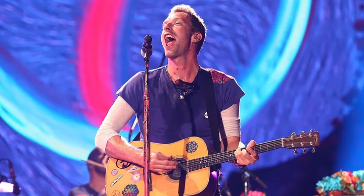 Lead singer playing guitar on stage with a vibrant background.