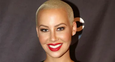 A person with short blonde hair smiling, wearing red lipstick.