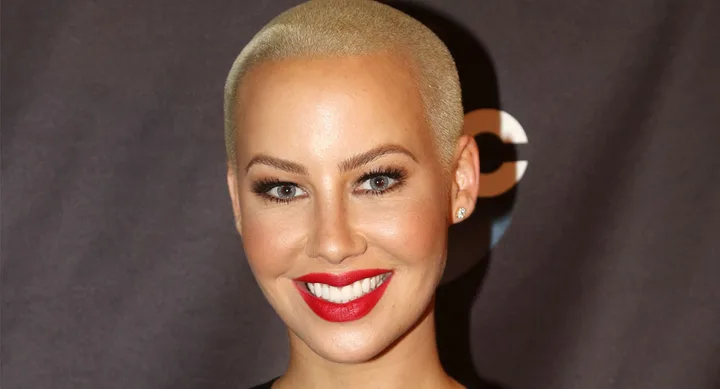 A person with short blonde hair smiling, wearing red lipstick.