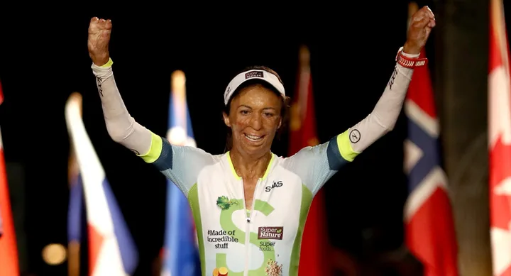 Triathlete celebrating with arms raised, wearing a "Made of incredible stuff" kit, flags in the background.