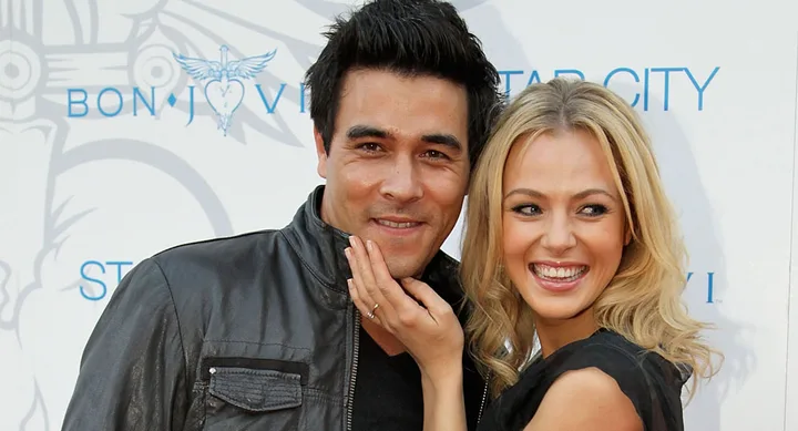Two smiling people pose together at a Bon Jovi event, with a backdrop featuring the band's logo.
