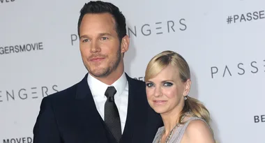 A suited man and a woman in a dress pose together at a "Passengers" event backdrop.