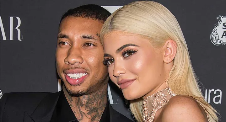 Two people smiling at an event with a dark background, one with blonde hair and the other with short hair and tattoos.