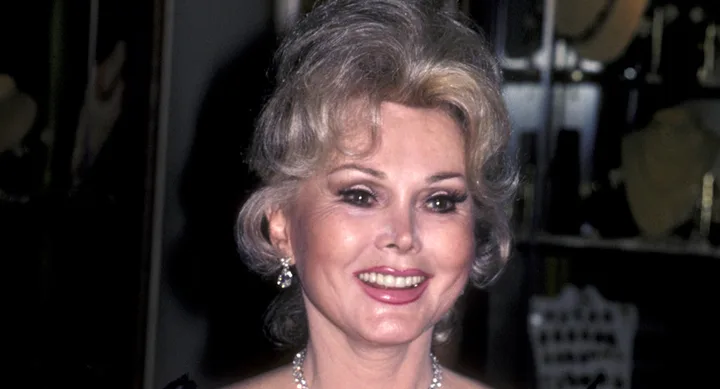 A woman with short blonde hair and earrings smiles in an elegant setting.