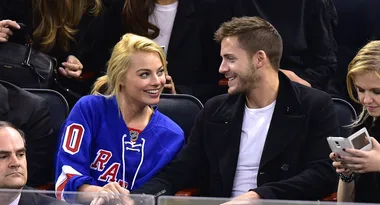 Margot Robbie and Tom Ackerley sitting in the crowd at a basketball game.