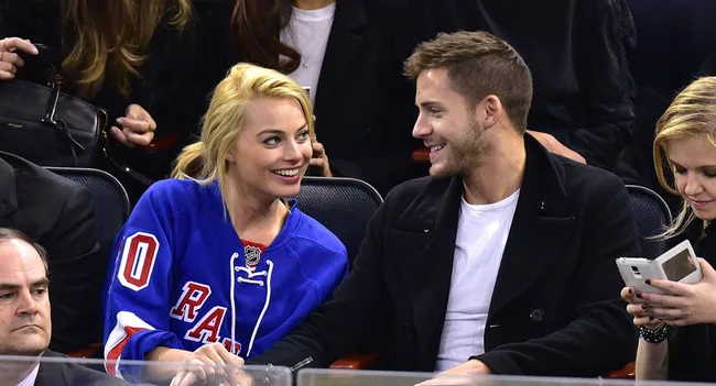 Margot Robbie and Tom Ackerley sitting in the crowd at a basketball game.