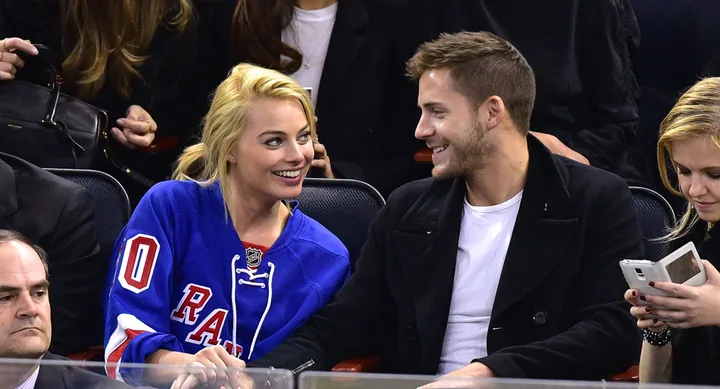 Margot Robbie and Tom Ackerley sitting in the crowd at a basketball game.