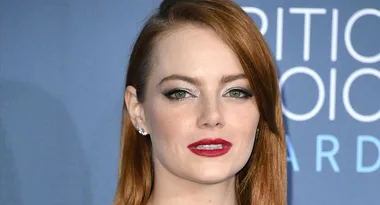 A person with red hair and red lipstick at a formal event with a blue background.