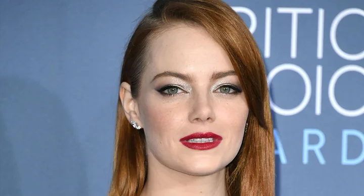 A person with red hair and red lipstick at a formal event with a blue background.