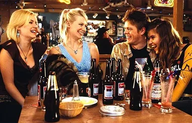 Friends laughing at a pub table with drinks and empty bottles, creating a joyful and lively atmosphere.