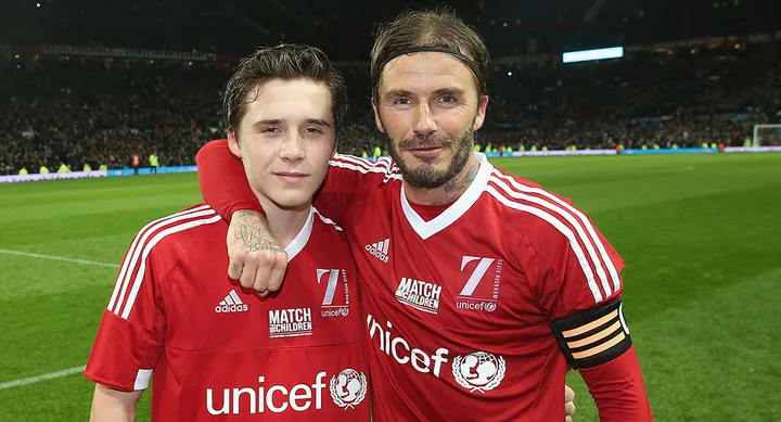 Two soccer players in red jerseys on a field, with arms around each other, smiling at the camera.