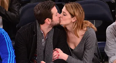 A couple kissing while seated in a sports arena, holding hands, with empty seats in the background.