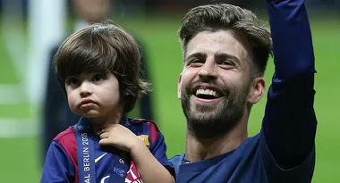 Footballer celebrating with a child wearing a FC Barcelona jersey and a Champions League 2015 medal.