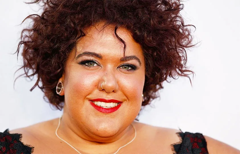 Curly-haired woman with a nose ring and red lipstick smiling at the camera.