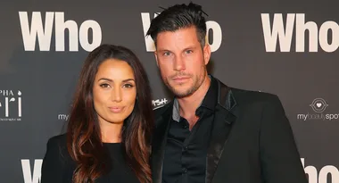 Two people posing on a red carpet in front of a backdrop with the word "Who" repeated multiple times.