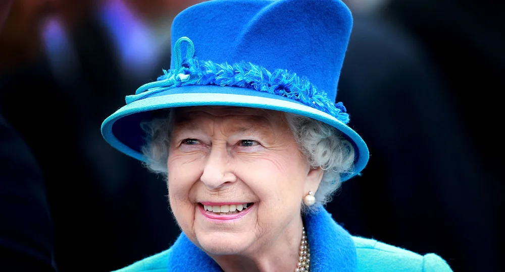 An elderly woman in a blue hat and coat, smiling.
