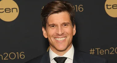 Man in suit smiling at a "Ten" event with logos in the background.
