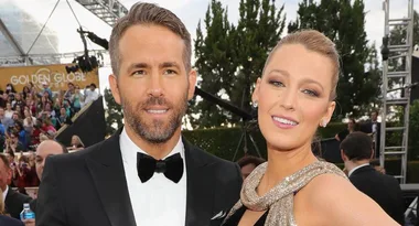 A couple posing on the red carpet at the Golden Globe Awards, surrounded by a crowd and trees in the background.