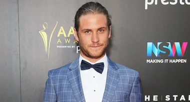 Man in a blue checkered suit and bow tie at an award event backdrop.