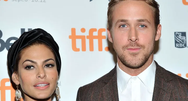 Two people pose in front of a TIFF backdrop, one wears a dark headwrap, the other a suit.