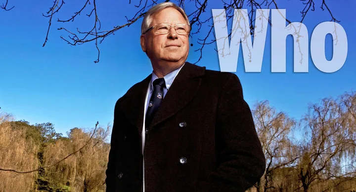 Man in overcoat outdoors, clear sky background, large "Who" text.