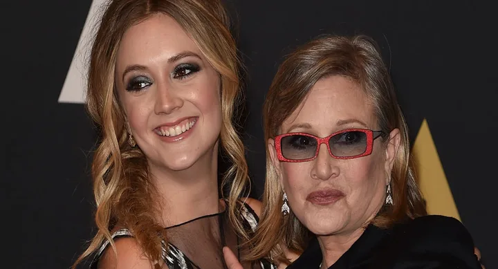 Two women smiling at an event, one wearing red glasses, both elegantly dressed, against a dark backdrop.