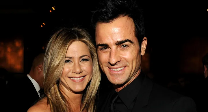 A smiling woman and man pose together at an event, both wearing dark attire.