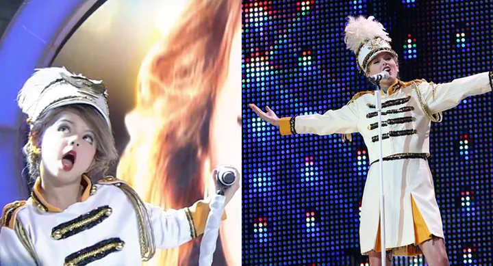 Child in a marching band uniform performs energetically with a microphone on stage.