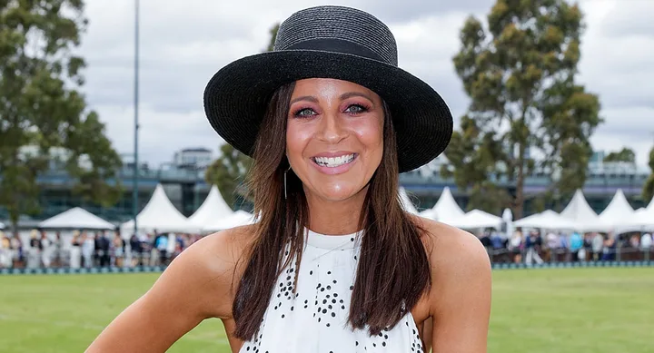 Woman in a wide-brimmed black hat and polka dot dress smiling at an outdoor event.