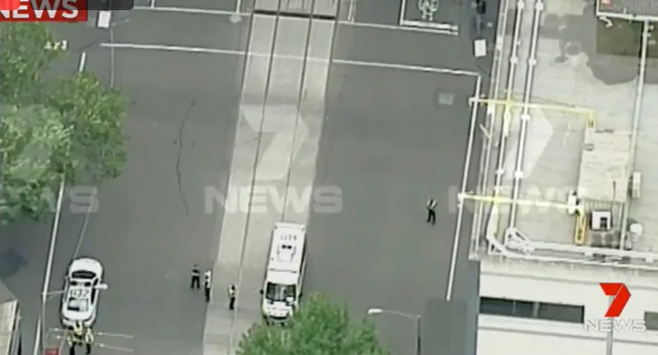 Aerial view of a city street blocked by police cars, with officers present and buildings surrounding the area.