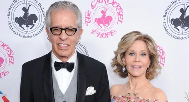 Two people posing at the Carousel of Hope event; the man wears glasses and a bow tie, the woman wears a floral gown.
