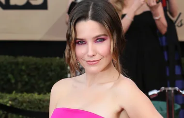A woman in a pink strapless dress poses at an event, with pink eyeshadow and styled brown hair.
