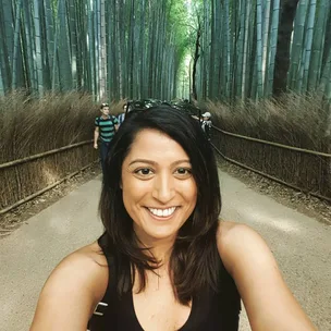 Selfie of a woman smiling in a bamboo forest pathway with people walking behind her.