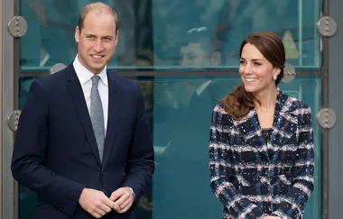Man in a suit and woman in a plaid coat smiling, standing outside a glass building.