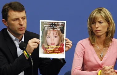 A man holds a poster about missing child, while a woman sits beside him at a press conference.