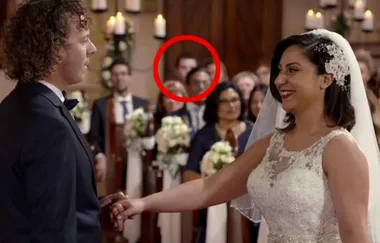 Bride and groom smile during wedding ceremony; guests seated in background, one circled in red smiling.