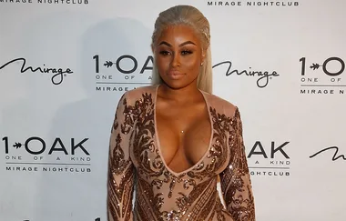 A person in a detailed, sequined dress poses at a nightclub event backdrop.