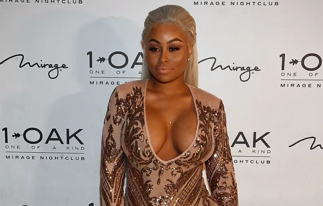 A person in a detailed, sequined dress poses at a nightclub event backdrop.