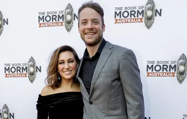 A smiling woman and man pose together at "The Book of Mormon" Australia event backdrop.