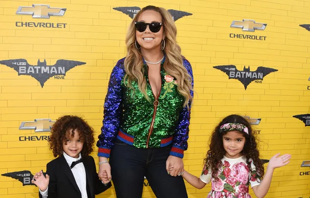 Singer in sunglasses with two young children at "The Lego Batman Movie" premiere, posed against a yellow background.