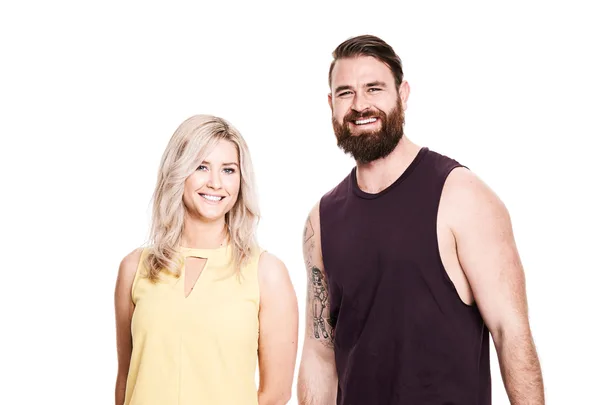 Man in a sleeveless black shirt and woman in a yellow top smiling at the camera against a white background.
