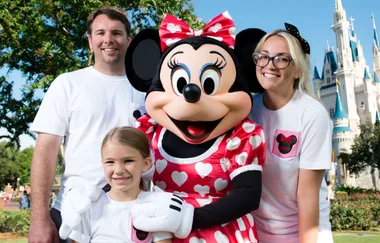A family poses with Minnie Mouse in front of Cinderella Castle at a Disney park.