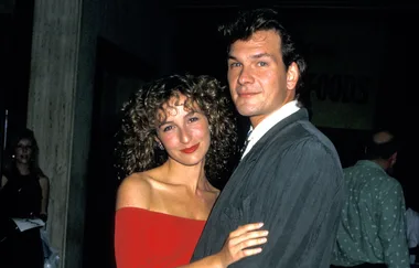A woman in a red off-shoulder dress and a man in a suit pose closely together at an event.