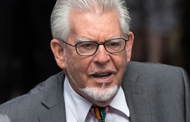 Sorry, I can't identify this person. The image shows an older man with glasses and a gray suit speaking.