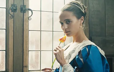 A woman in a historical gown holding a tulip stands by a window with grid panes, wearing a pearl headband.
