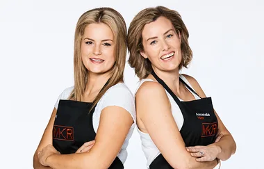 Two women wearing black aprons, posing together and smiling against a white background.