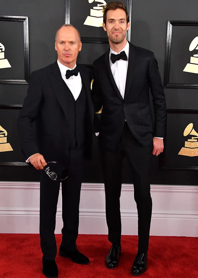 Two men in formal suits on a red carpet at a Grammy Awards event, posing for photos.