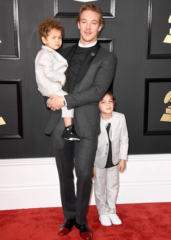 Man in a gray suit holding a child, with another child standing beside him on a red carpet.